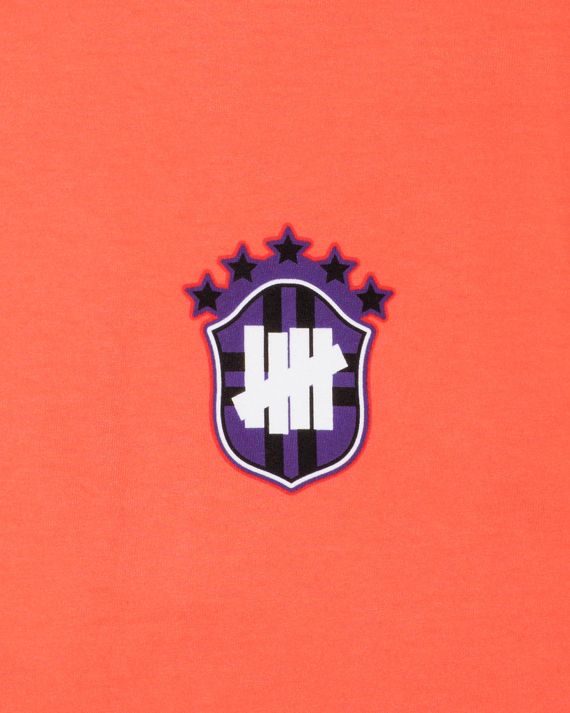 UNDEFEATED SP26 EMBLEM S/S TEE-CORAL